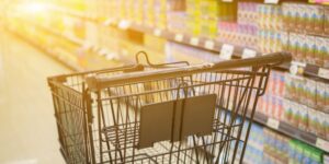 An empty shopping trolley in a supermarket aisle next to full shelves.