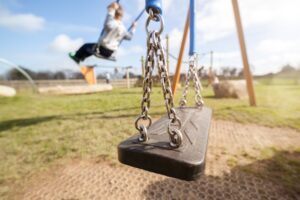 Children play on a swing set in a grassy park