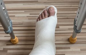 A man's foot in a white cast resting on the ground bracketed by two crutches.