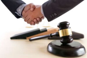 A solicitor and client shake hands over a gavel and case files after they sue for a criminal injury.