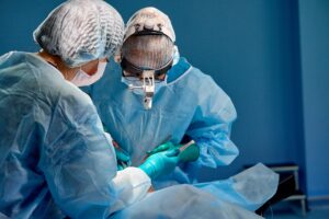 A surgeon and a nurse in blue surgical scrubs, looking down towards a patient.