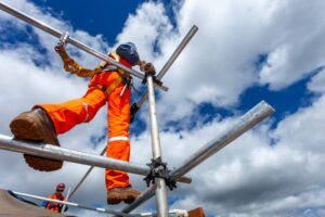 A scaffolding worker wearing orange overalls stood on some scaffolding. 