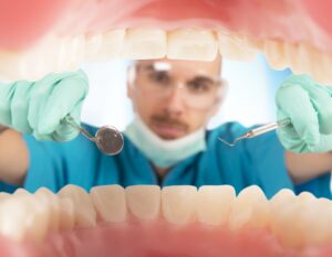 A dentist holding a small mirror, from the perspective of inside a patient's mouth.