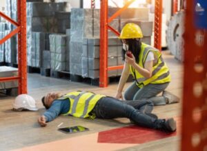 A warehouse worker holding a walkie talkie and helping an injured co-worker lying on the floor