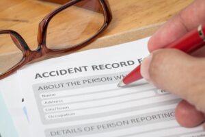 CLOSE UP OF A PERSON COMPLETING AN ACCIDENT AT WORK PERSONAL INJURY CLAIM REPORT 