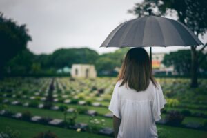 A young woman holding up an open umbrella at a graveyard