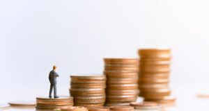 Small piles of coins with a plastic figurine of a person stood on the smallest pile.