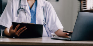 Medical professional looking at notes on screen and paper.